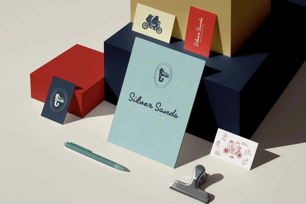 Business cards and a note card in blue, red and cream, stacked on colored boxes beside a pen and a clip